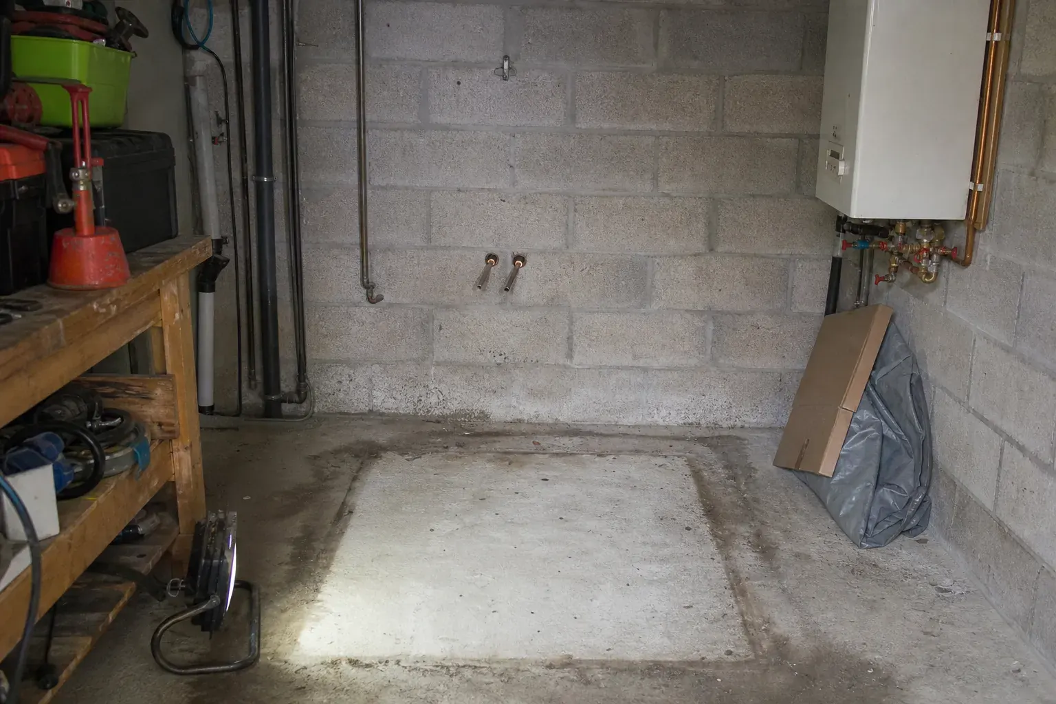 Empreinte au sol d’une cuve retirée dans un local technique, avec deux attentes de canalisation coupées et bouchonnées au mur