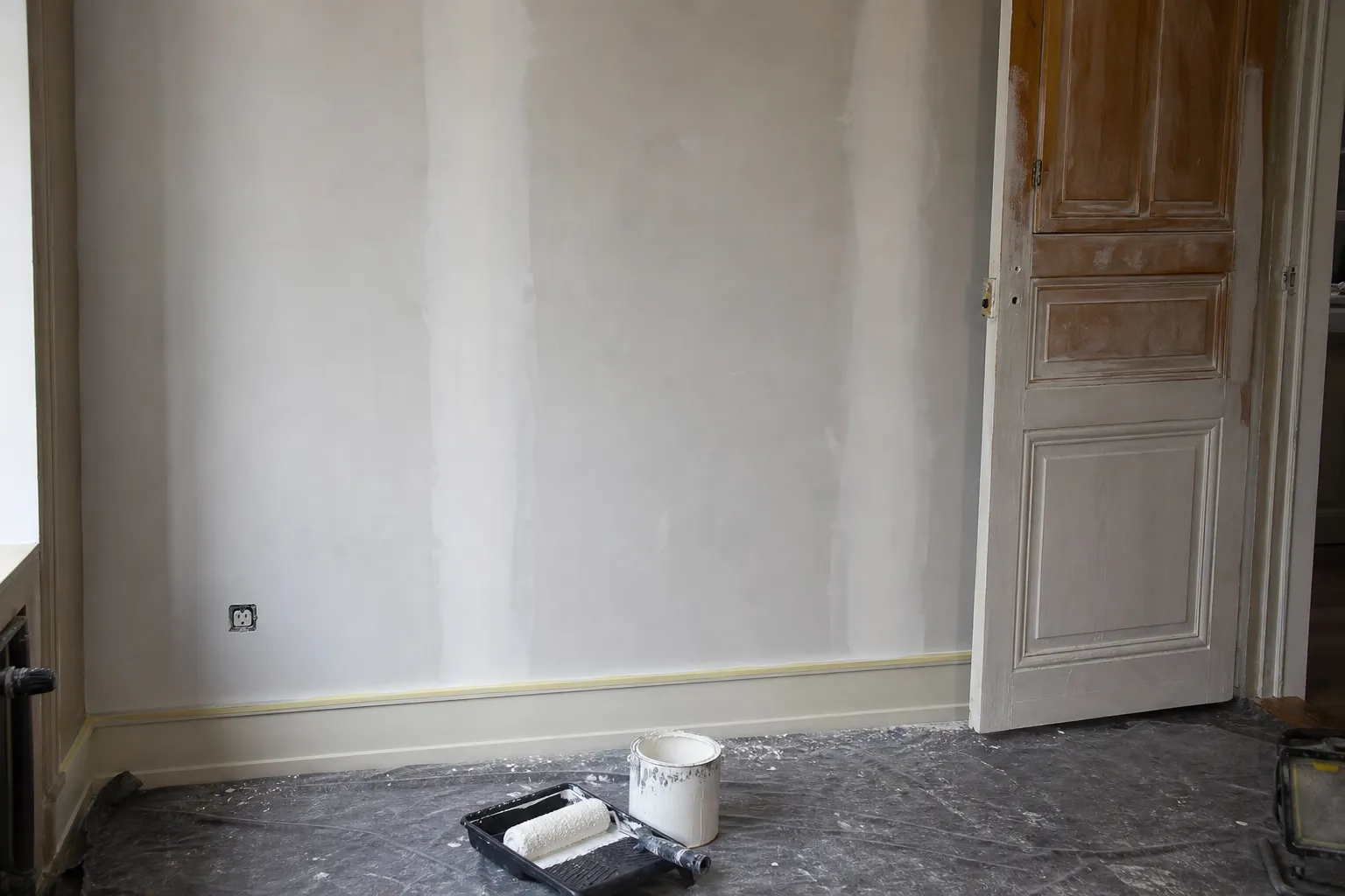 Mur repris en peinture dans un logement ancien, bandes de joint poncées visibles et huisserie repeinte à moitié