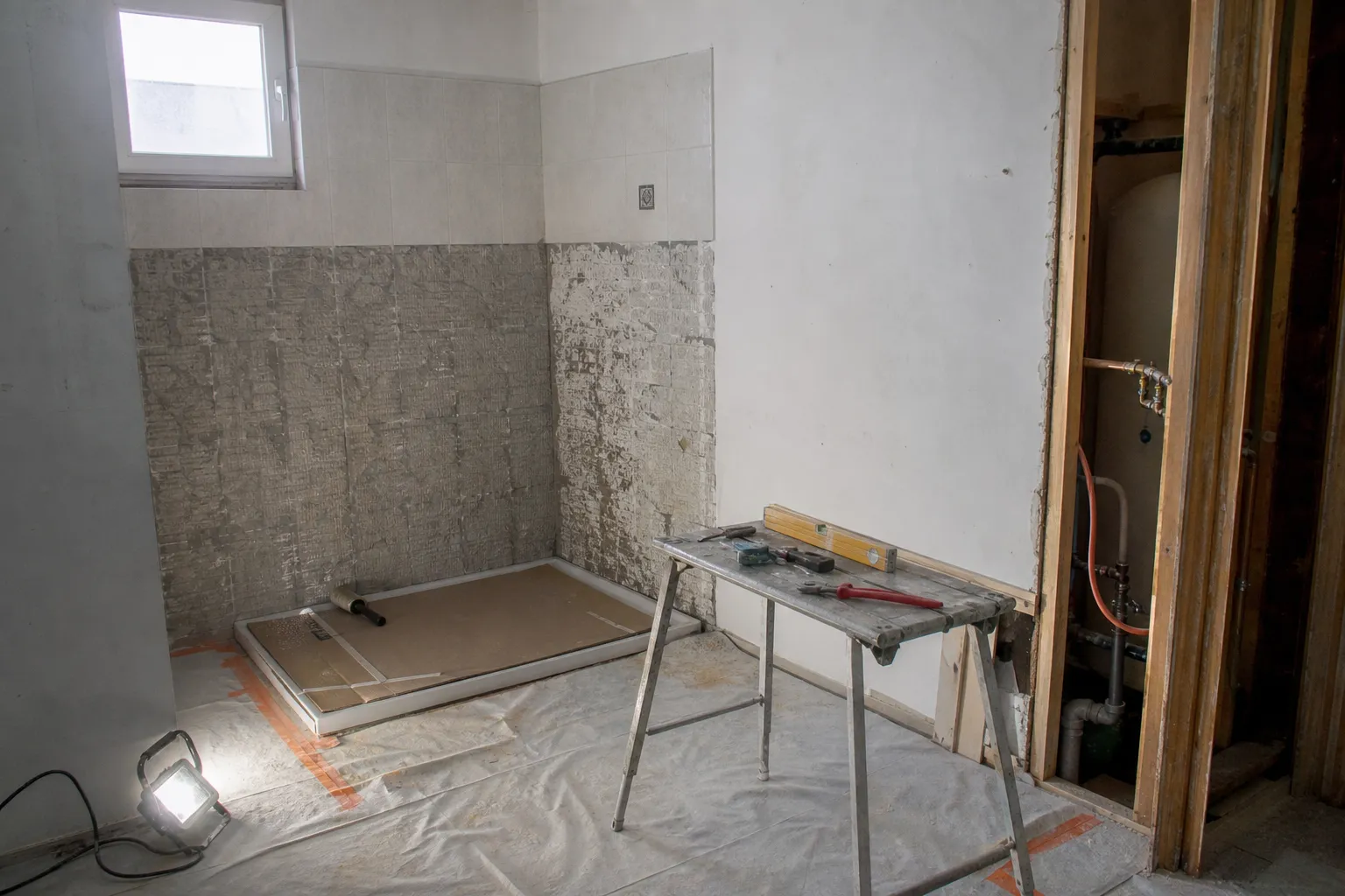 Salle de bain en travaux, cloison ouverte sur l’attente d’eau chaude et le vide réservé au ballon, receveur protégé au sol