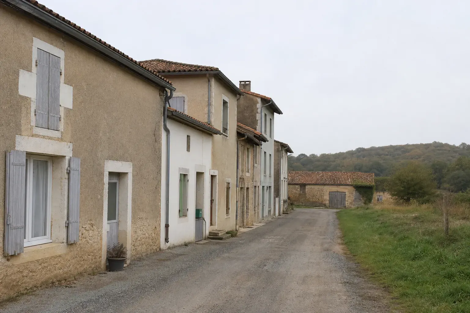 Rue de bourg rural mêlant maisons anciennes enduites et pavillons récents, grange basse en bout de rangée